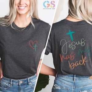 May include: A dark heather grey t-shirt with a small heart and cross design on the left chest and the text "Jesus has my back" with a cross on the back.