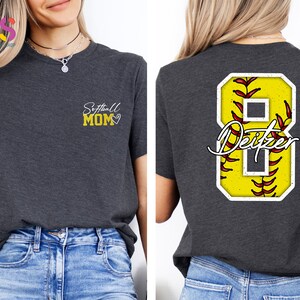 May include: A dark grey t-shirt with the text "Softball Mom" and a heart on the left chest. The back of the shirt has a yellow softball with red stitching and the number 8 with the name "Deitzel" written in white.