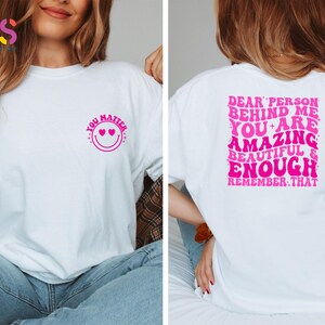 May include: White t-shirt with a pink smiley face with hearts for eyes and the text "You Matter" on the front. The back of the shirt has the text "Dear person behind me, you are amazing, beautiful & enough. Remember that." in pink.