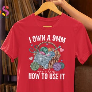 May include: Red t-shirt with a white graphic of a basket of yarn and knitting needles. The text "I own a 9mm and I know how to use it" is printed on the shirt.