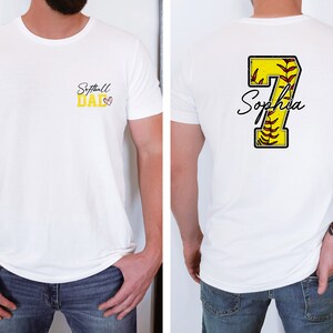 May include: White t-shirt with the text "Softball Dad" on the front and a yellow softball with the number 7 and the name "Sophia" on the back.