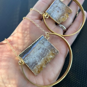 May include: Two gold necklaces with a large, rectangular, clear, and yellow agate stone pendant. The stones have a layered, crystal-like appearance. The necklaces have a simple, gold chain and a gold hoop.
