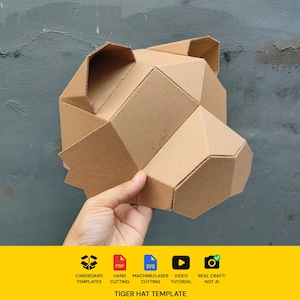 Könnte beinhalten: Eine geometrische Tigerhut-Vorlage aus brauner Wellpappe. Die Struktur besteht aus kantigen, facettierten Flächen, die eine stilisierte Tierkopfform mit zwei spitzen Ohren und einem hervorstehenden Schnauzenbereich bilden, konzipiert für den Zusammenbau.