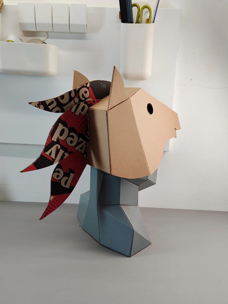 Puede incluir: Una escultura geom&eacute;trica de cabeza de caballo hecha de cart&oacute;n color canela con una melena de papel estampada en rojo oscuro y negro que presenta texto impreso. La secci&oacute;n del cuello y el pecho est&aacute; hecha de paneles geom&eacute;tricos gris claro.