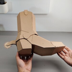 Puede incluir: Una escultura tridimensional de bota vaquera construida con cart&oacute;n marr&oacute;n. La bota presenta un dise&ntilde;o geom&eacute;trico y facetado con una espuela prominente unida al tal&oacute;n, mostrando l&iacute;neas limpias y angulares con una estructura de papel.