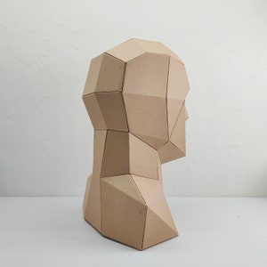 May include: A geometric sculpture of a human head made from cardboard. The sculpture is brown and has a faceted design.