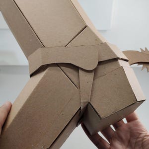 Puede incluir: Un modelo de bota vaquera hecho de cart&oacute;n marr&oacute;n que presenta una espuela prominente unida al &aacute;rea del tal&oacute;n. La estructura est&aacute; construida con paneles de cart&oacute;n plegados, mostrando un dise&ntilde;o geom&eacute;trico que imita la forma de una bota.