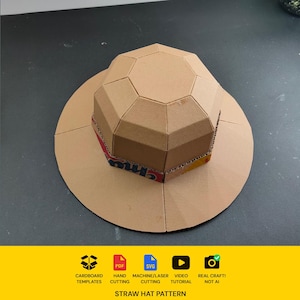 May include: A tan cardboard hat constructed from geometric panels with a wide circular brim. The base of the crown features a band with red and yellow printed text. Below the hat, icons indicate cardboard templates, PDF, SVG, machine cutting, video tutorial, and real craft, with the text STRAW HAT PATTERN.