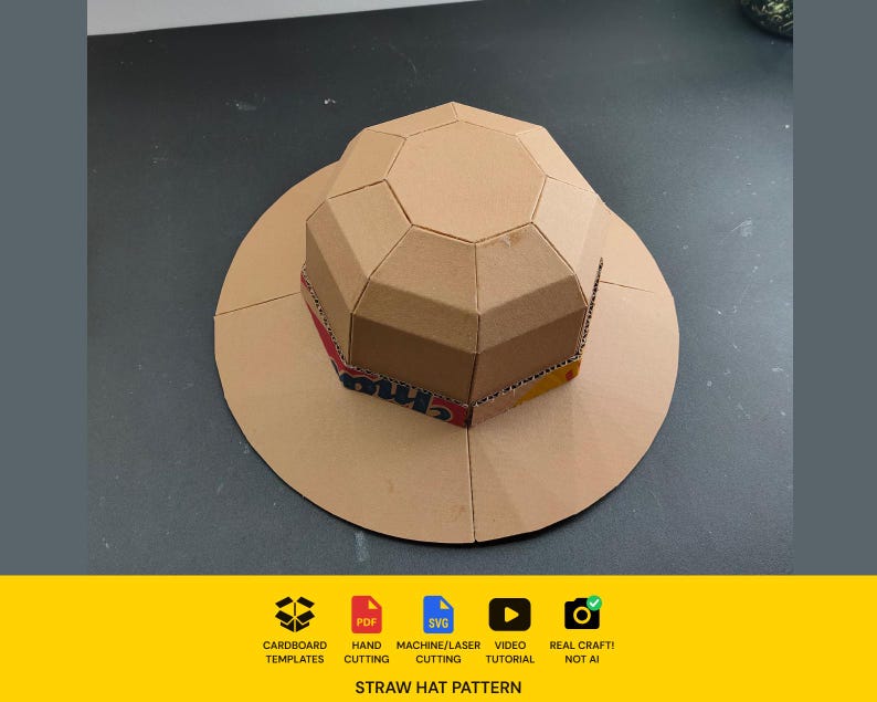 May include: A tan cardboard hat constructed from geometric panels with a wide circular brim. The base of the crown features a band with red and yellow printed text. Below the hat, icons indicate cardboard templates, PDF, SVG, machine cutting, video tutorial, and real craft, with the text STRAW HAT PATTERN.