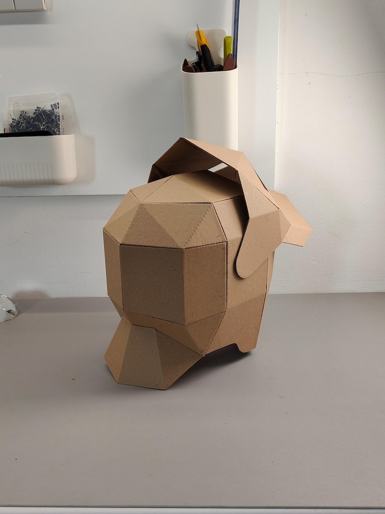 May include: A geometric, brown cardboard sculpture of a dog's head and body. The sculpture is made of folded cardboard pieces, creating a faceted appearance. The dog's head has a flap that serves as an ear.