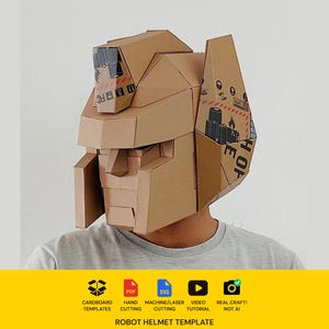 May include: A brown cardboard robot helmet constructed from folded panels with geometric features, including a central crest, side fins, and a visor-like face plate. The material displays visible printed shipping icons and text on the side panels.