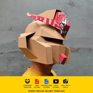 May include: A cardboard robot mecha helmet featuring geometric panels and a red and white patterned accent piece on the forehead and chin. The helmet has a structured visor area and side ear components, constructed from brown corrugated material.