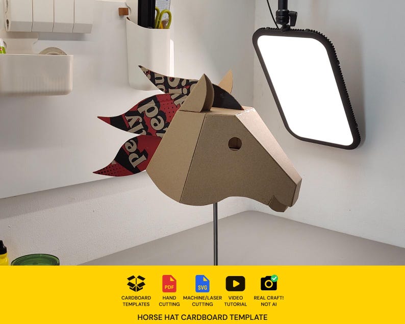 Puede incluir: Una m&aacute;scara de cabeza de caballo de cart&oacute;n con dise&ntilde;o geom&eacute;trico y una crin con estampado rojo, negro y blanco. La m&aacute;scara est&aacute; montada sobre un soporte met&aacute;lico fino. Debajo, una franja amarilla muestra iconos de archivos PDF, SVG y tutorial.