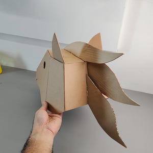 Puede incluir: Una escultura geom&eacute;trica de cabeza de caballo construida con cart&oacute;n corrugado marr&oacute;n. El dise&ntilde;o presenta un hocico facetado, un ojo circular recortado, una oreja puntiaguda y una crin fluida compuesta por segmentos de cart&oacute;n curvos y superpuestos.