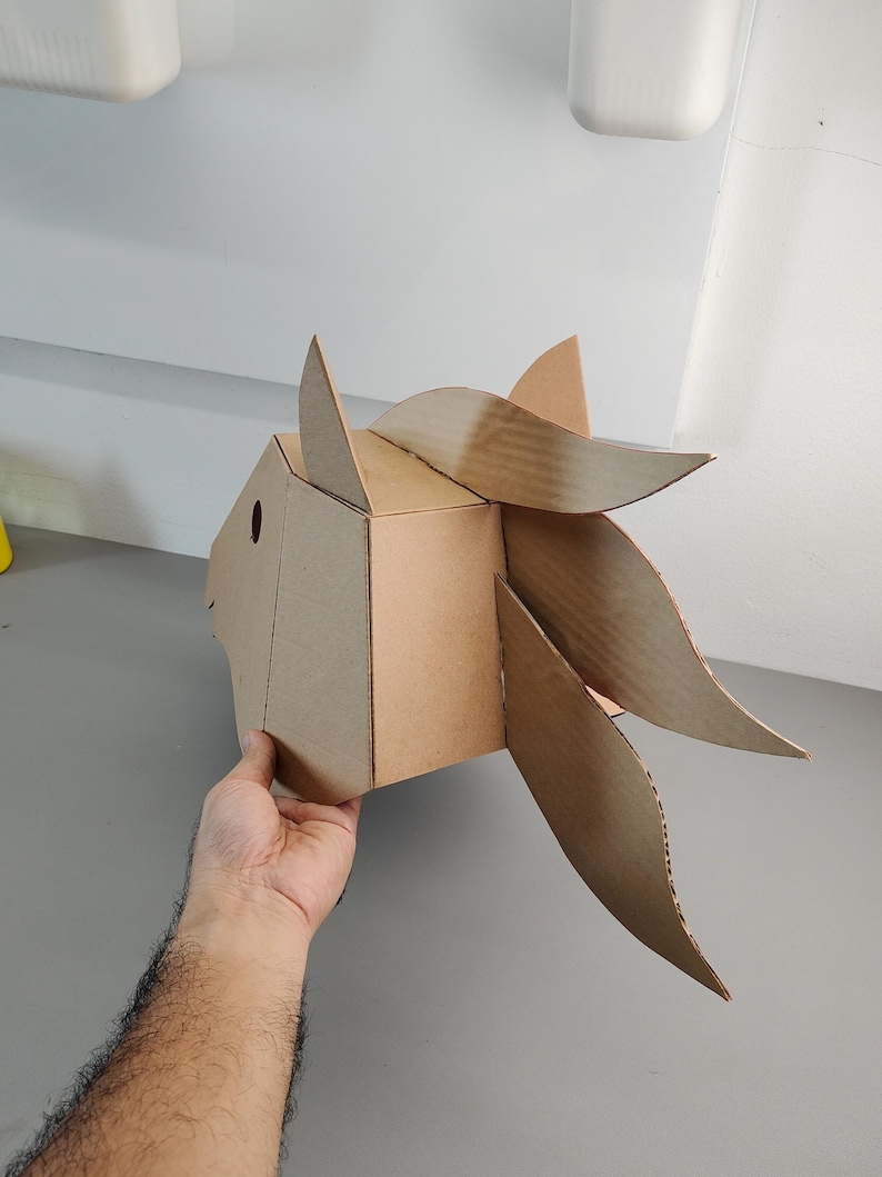 Puede incluir: Una escultura geom&eacute;trica de cabeza de caballo construida con cart&oacute;n corrugado marr&oacute;n. El dise&ntilde;o presenta un hocico facetado, un ojo circular recortado, una oreja puntiaguda y una crin fluida compuesta por segmentos de cart&oacute;n curvos y superpuestos.