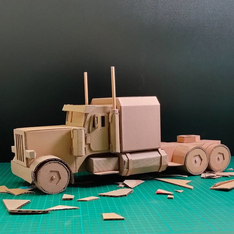 Pode incluir: Um modelo de cami&atilde;o de plataforma com reboque feito de cart&atilde;o. O cami&atilde;o &eacute; castanho e tem uma cabina e rodas detalhadas. O reboque tamb&eacute;m &eacute; castanho e tem um design simples.