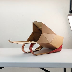 May include: A cardboard box shaped like a spaceship with red and white text that says "Boston Pizza" on the side.