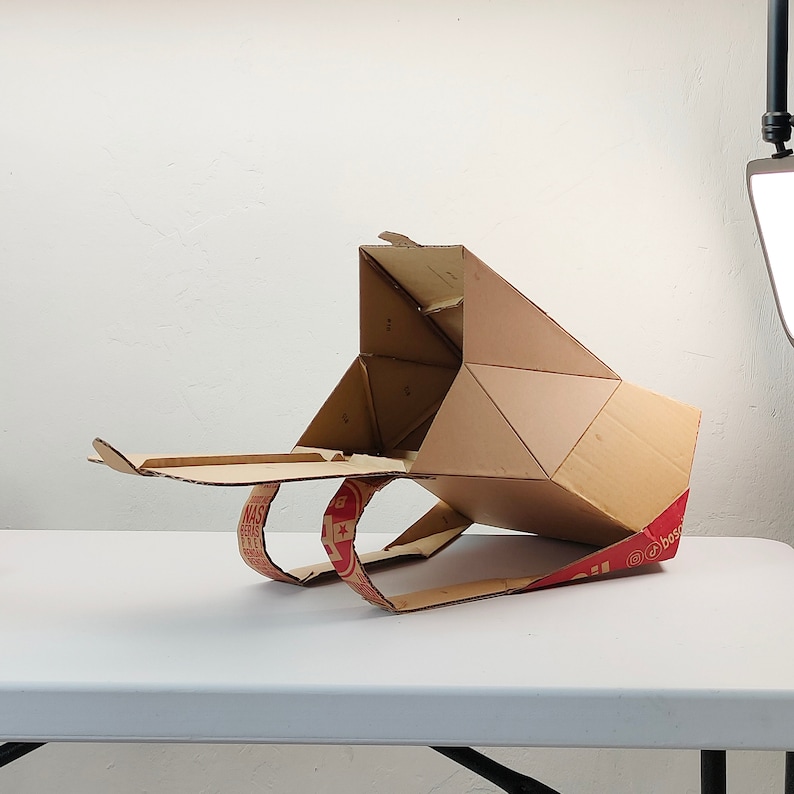 May include: A cardboard box shaped like a spaceship with red and white text that says "Boston Pizza" on the side.