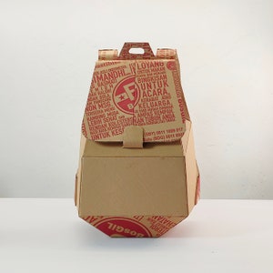 May include: A brown cardboard box with a red and white logo that says "Jastibisa" and "Imanidhi". The box has a handle on the top and is designed for takeaway food. The box has text in Indonesian.