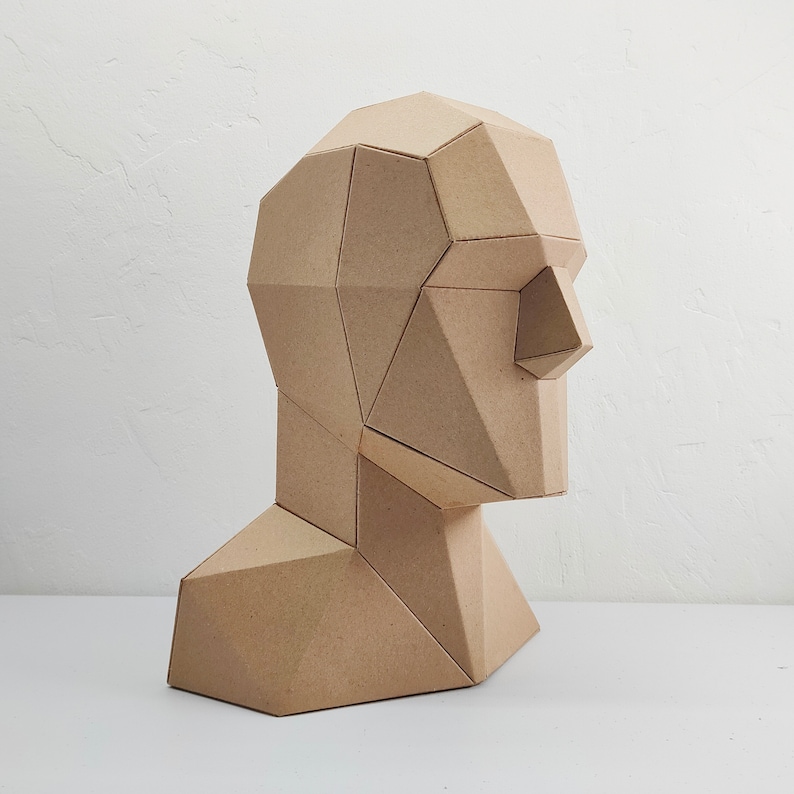 May include: A brown cardboard sculpture of a human head and neck, with a geometric design. The sculpture is made of many flat, angular pieces of cardboard.