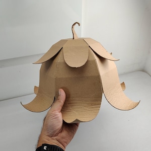 May include: A bell-shaped structure constructed from brown corrugated cardboard, featuring multiple overlapping petal-like segments arranged in two tiers and a small curved stem-like protrusion at the very top center of the object.