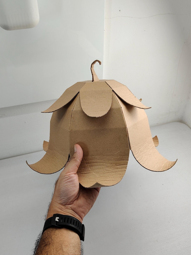May include: A bell-shaped structure constructed from brown corrugated cardboard, featuring multiple overlapping petal-like segments arranged in two tiers and a small curved stem-like protrusion at the very top center of the object.