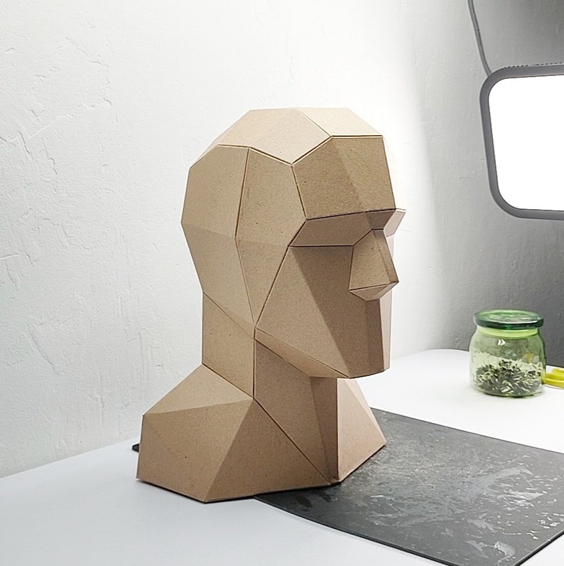 May include: A brown paper mache sculpture of a human head and neck, with a geometric design. The sculpture is made up of many polygons and is viewed from the side.