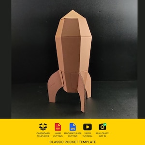 May include: A three-dimensional cardboard rocket model with a pointed nose cone and three stabilising fins. Below the rocket, a yellow banner displays icons for cardboard templates, PDF, SVG, machine/laser cutting, video tutorial, and real craft, with the text "CLASSIC ROCKET TEMPLATE".