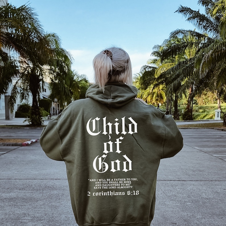 Pode incluir: Uma camisola de capuz verde com as palavras "Child of God" em letras brancas nas costas. O texto abaixo diz "And I will be a father to you, and you shall be sons and daughters to me, says the Lord Almighty, 2 Corinthians 6:18."