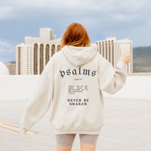 May include: A cream colored hoodie with a black print that says "psalms LXII:11" and "TRULY HE IS MY ROCK AND MY SALVATION; HE IS MY FORTRESS, I WILL NEVER BE SHAKEN".