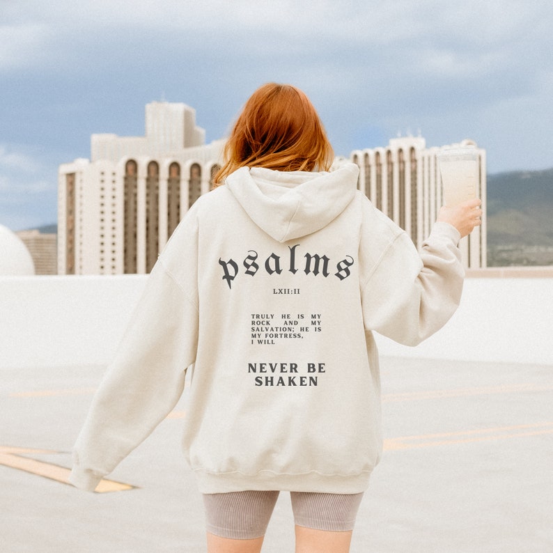 May include: A cream colored hoodie with a black print that says "psalms LXII:11" and "TRULY HE IS MY ROCK AND MY SALVATION; HE IS MY FORTRESS, I WILL NEVER BE SHAKEN".