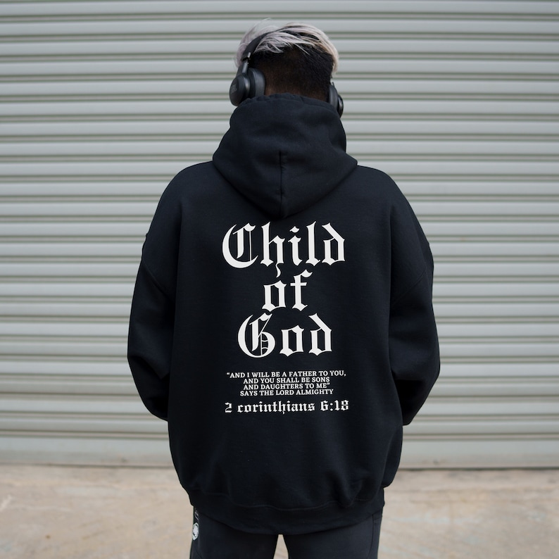 Pode incluir: Camisola de moletom com capuz preta com o texto "Child of God" e um vers&iacute;culo b&iacute;blico de 2 Cor&iacute;ntios 6:18 impresso nas costas.