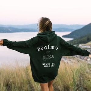 May include: A dark green hoodie with a white print that reads "psalms LX11:11" and "TRULY HE IS MY ROCK AND SALVATION; HE IS MY FORTRESS. I WILL NEVER BE SHAKEN".