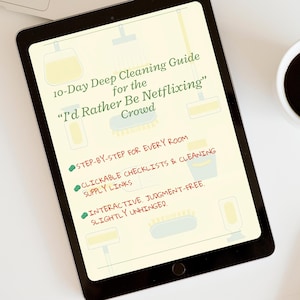 May include: A black tablet displays a cleaning guide titled "10-Day Deep Cleaning Guide for the 'I'd Rather Be Netflixing' Crowd." The guide includes step-by-step instructions, clickable checklists, and cleaning supply links. A cup of coffee sits to the right.