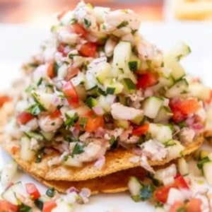 May include: A close-up of a tostada topped with a colorful ceviche made with fresh fish, tomatoes, onions, cilantro, and cucumbers.