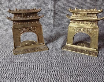 May include: A pair of gold-toned metal bookends shaped like traditional Chinese pagodas. The bookends have intricate details and are a decorative addition to any bookshelf.