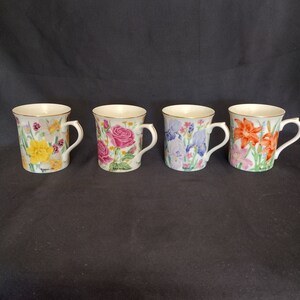 May include: Four white ceramic mugs with floral designs. Each mug features a different flower: daffodils, roses, irises, and lilies.