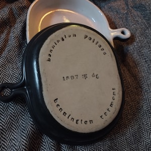 May include: A black cast iron skillet with a white interior and a white ceramic baking dish. The skillet has the words "Bonnairellium Vollone" and "1897 No 86" inscribed on the bottom. The baking dish has the words "Bonnairellium Vollone" inscribed on the bottom.