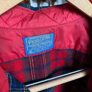 May include: A Pendleton jacket with a red quilted lining and a red, green, and blue plaid wool exterior. A blue rectangular label is stitched to the interior, reading: Warranted to be a Pendleton, Pendleton Woolen Mills, Portland, Oregon, 100% Virgin Wool, L, Pure Virgin Wool, Made in U.S.A.