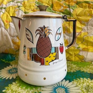 May include: White enamelware coffee pot with a gold rim and handle. The pot features a large brown pineapple illustration, along with other colorful fruit and leaf designs. The text "Georges Briard" is printed on the side.