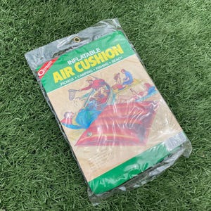 May include: An inflatable air cushion in its original packaging. The packaging is green and white with the words "INFLATABLE AIR CUSHION" and illustrations of people fishing, camping, and at the beach. The cushion itself is red.