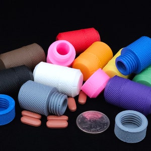 May include: Assortment of colorful pill containers with a textured finish. Some containers are open, revealing a white interior. A few brown pills are scattered around the containers.