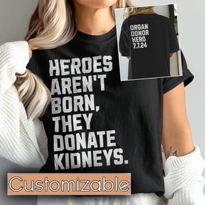 May include: Black t-shirt with white text that reads "HEROES AREN'T BORN, THEY DONATE KIDNEYS." The back of the shirt has white text that reads "ORGAN DONOR HERO 7.7.24". The shirt is customizable.