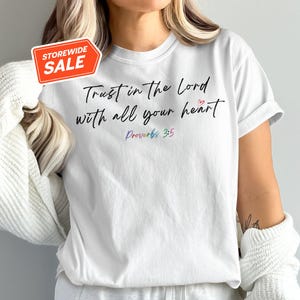 Puede incluir: Camiseta blanca con el texto "Trust in the Lord with all your heart" y "Proverbs 3:5" en letras de colores.
