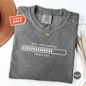 May include: Grey t-shirt with a white loading bar graphic that says "Stem cells updating... Please wait..."