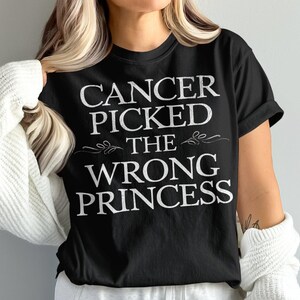 May include: Black t-shirt with white text that reads "Cancer picked the wrong princess".