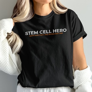 May include: Black t-shirt with the text "STEM CELL HERO" and the phrase "Heroes aren't born, they donate stem cells" in white text.