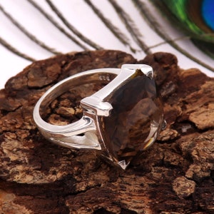 Op de afbeelding: Zilveren ring met een grote, bruine, marquise-geslepen rookkwarts edelsteen. De ring heeft een gedetailleerd ontwerp aan de zijkanten. De edelsteen heeft een diepe bruine kleur. Geplaatst op een houten oppervlak.
