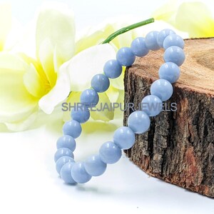 Könnte beinhalten: Ein hellblaues Edelstein-Armband mit runden Perlen. Das Armband liegt auf einer Holzoberfläche.