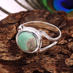 May include: A silver ring with a green gemstone set in a round bezel. The ring has a delicate, openwork design on the band.